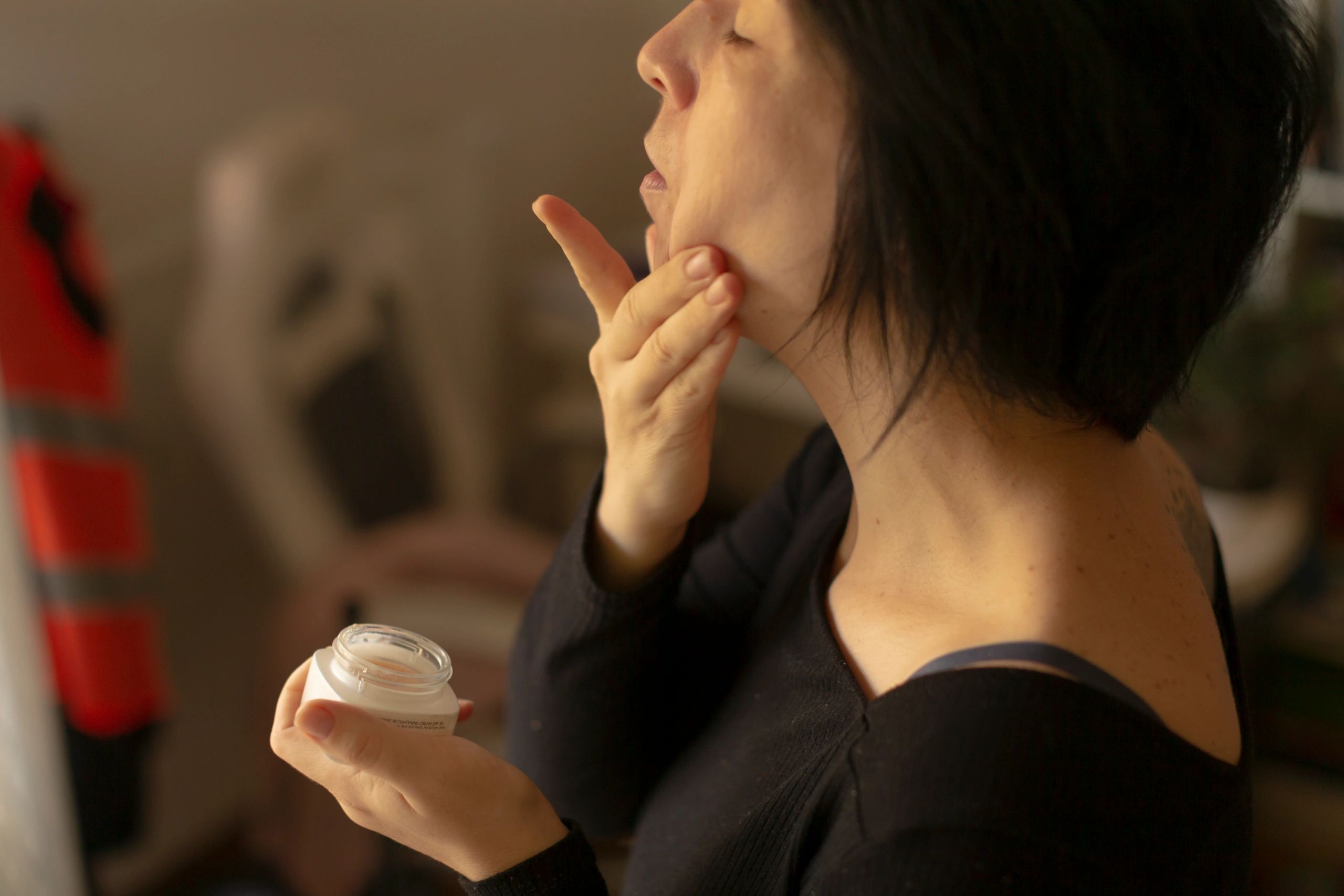 Woman applying moisturizer to neck and jawline, illustrating skincare and contour focus
